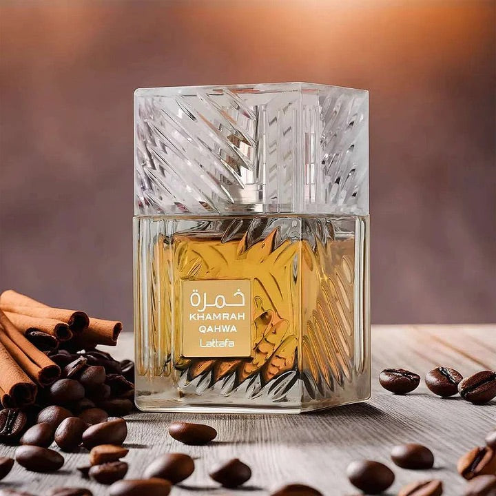 Glass perfume bottle labeled 'Khamrah Qahwa Latte' with coffee beans and cinnamon sticks on a wooden surface.